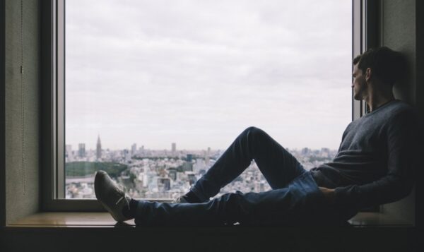 Man sat in a window looking over a city with depressed body language