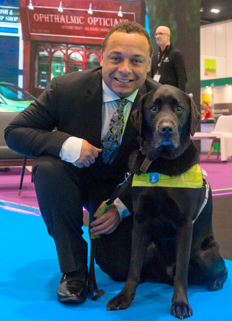 Daniel with his best friend - his black labrador guide dog Zodiac. Together they travel the length and breadth of the UK to increase inclusion and accessibility for people with visual impairments. Dan is wearing a suit and Zodiac has his working harness on.